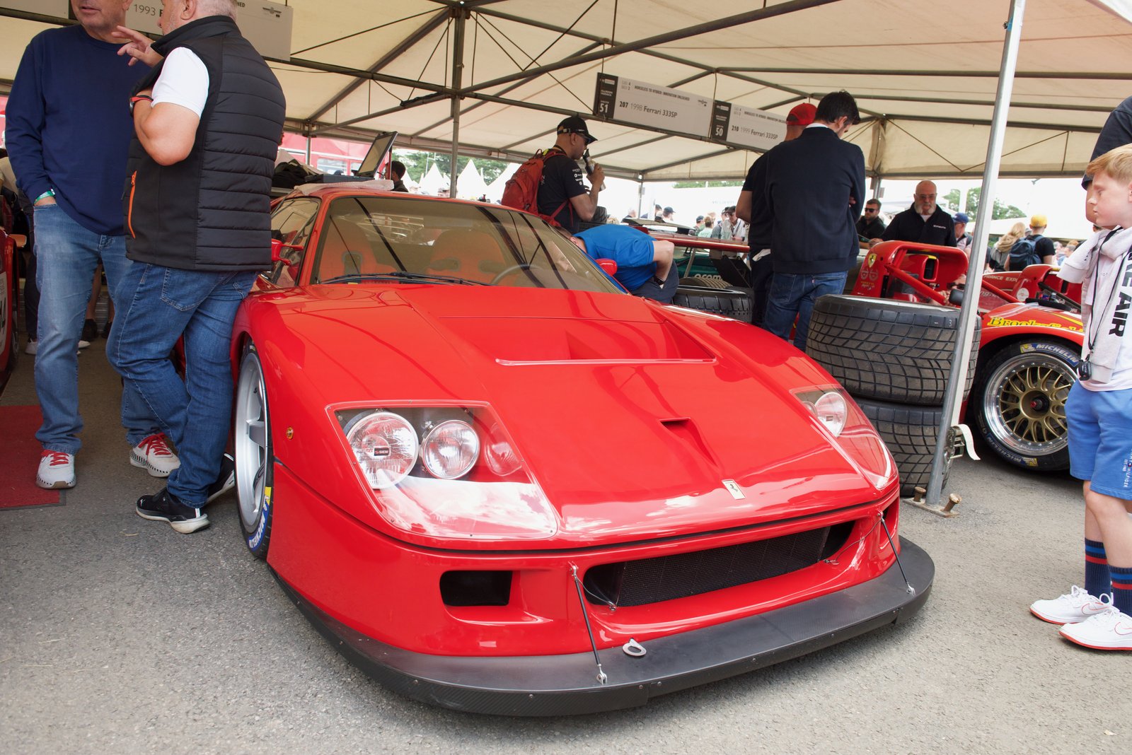 Ferrari F40 LM rossa nel paddock di un evento di corse storiche, circondata dagli appassionati
